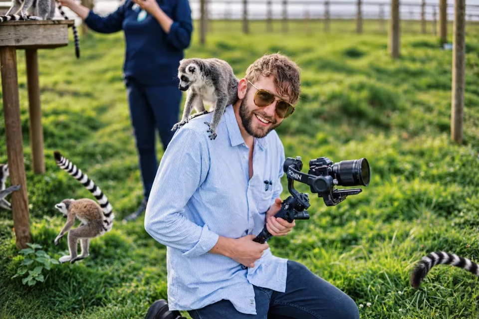 Sam holding a camera stabiliser with a ring-tailed lemur on his shoulder