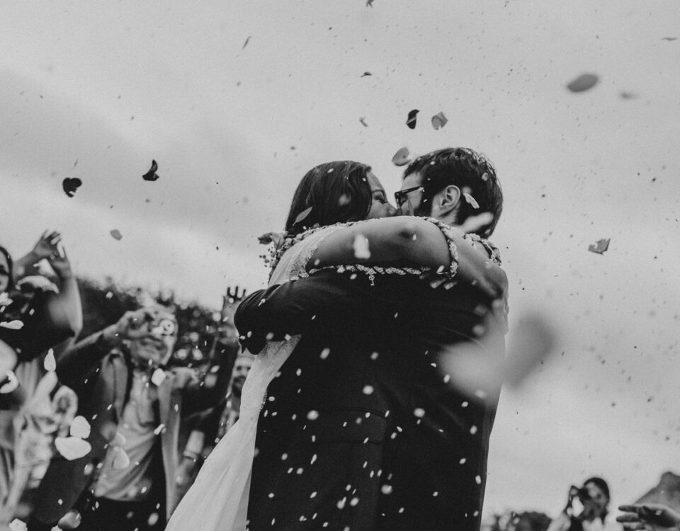 Bride and groom embrace in a shower of flower petals during their outdoor wedding ceremony