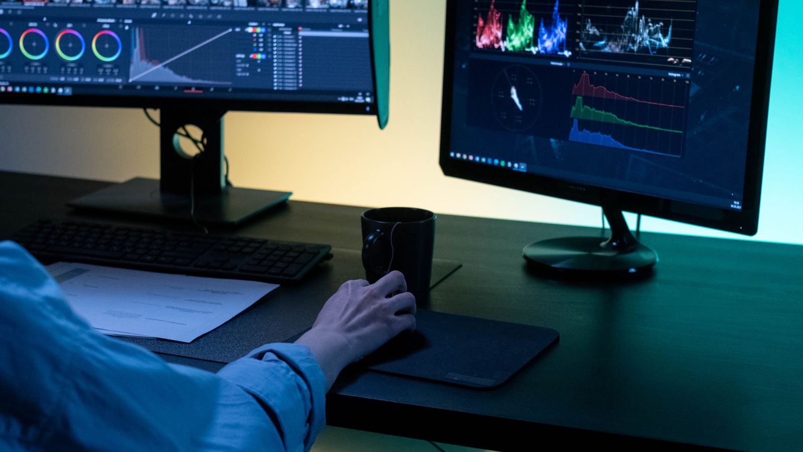 A video editor works on dual monitors in a modern setup, focusing on color grading and editing visuals
