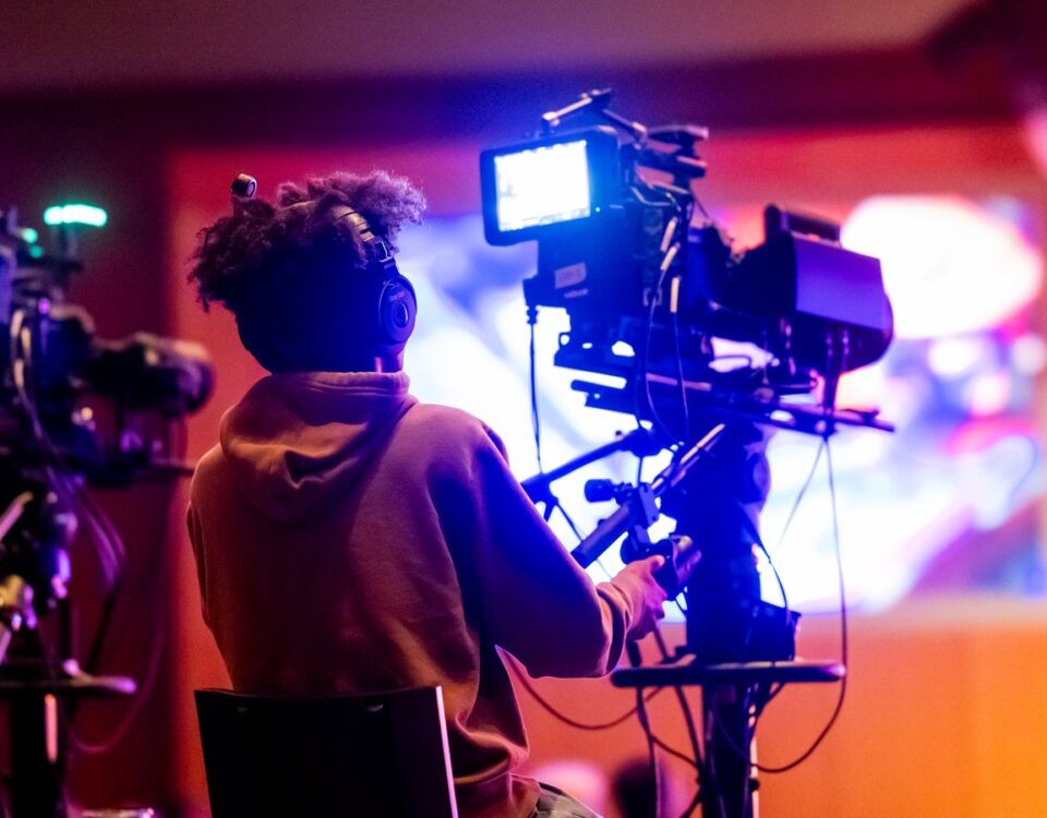 Back view of a videographer operating a camera at a live event, focusing on a vibrant indoor setup