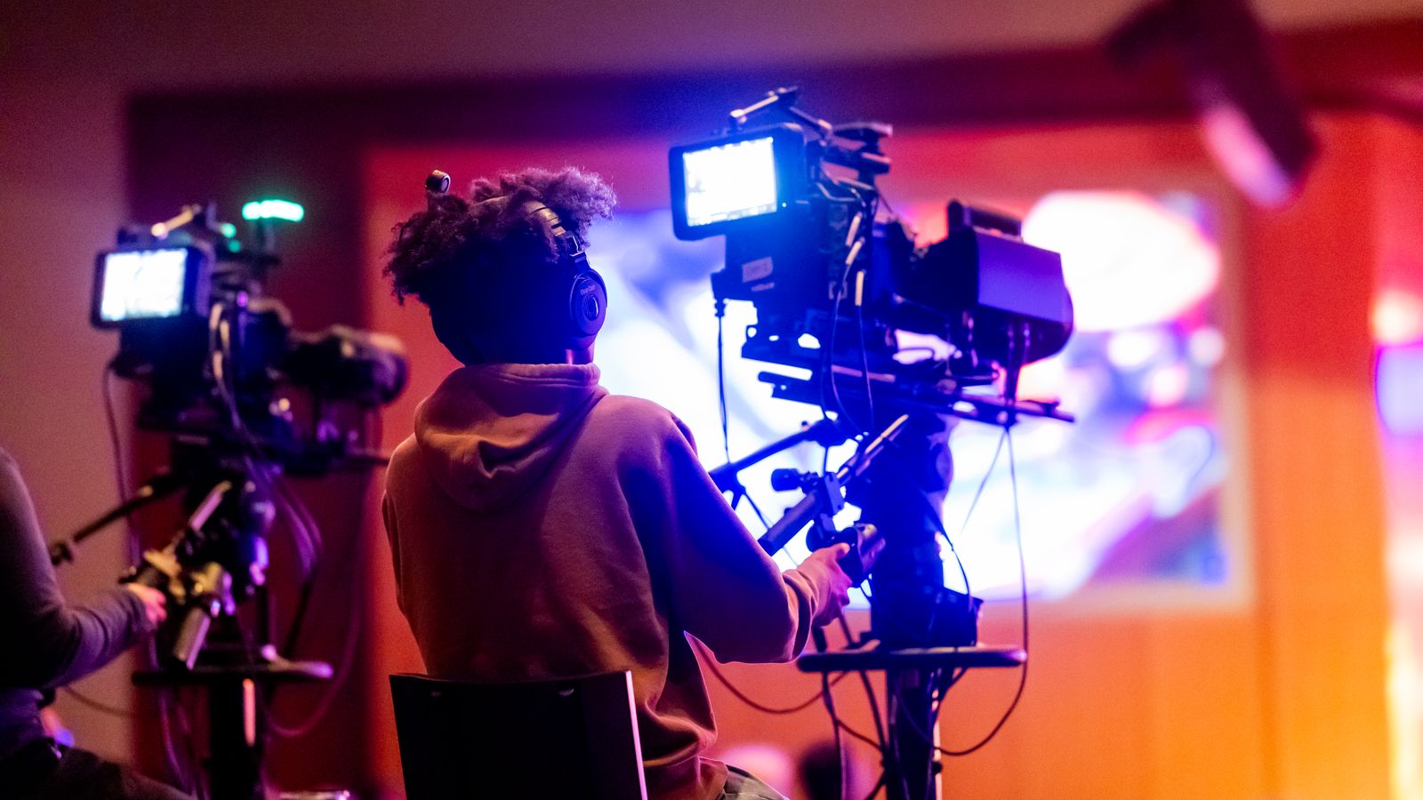 Back view of a videographer operating a camera at a live event, focusing on a vibrant indoor setup