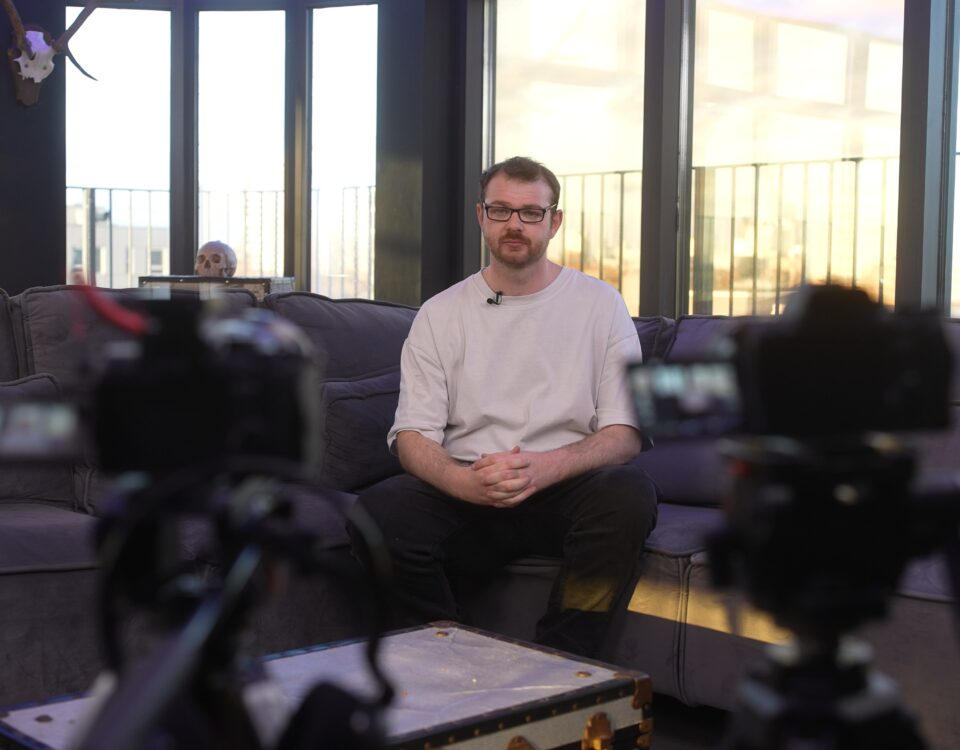 Two cameras filming a seated speaker in a lounge setting