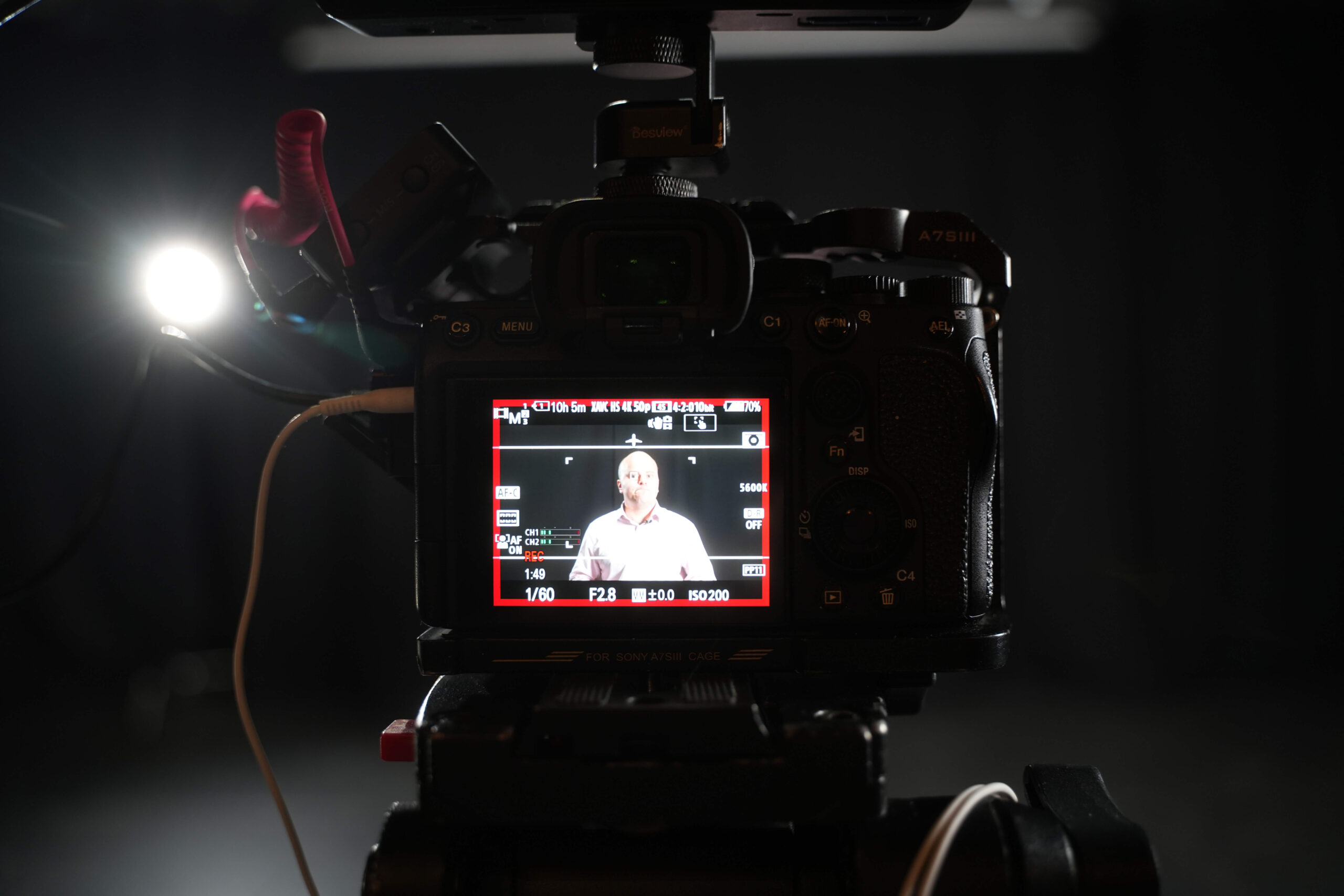 Cinema camera monitor showing a seated interview subject in a dark studio