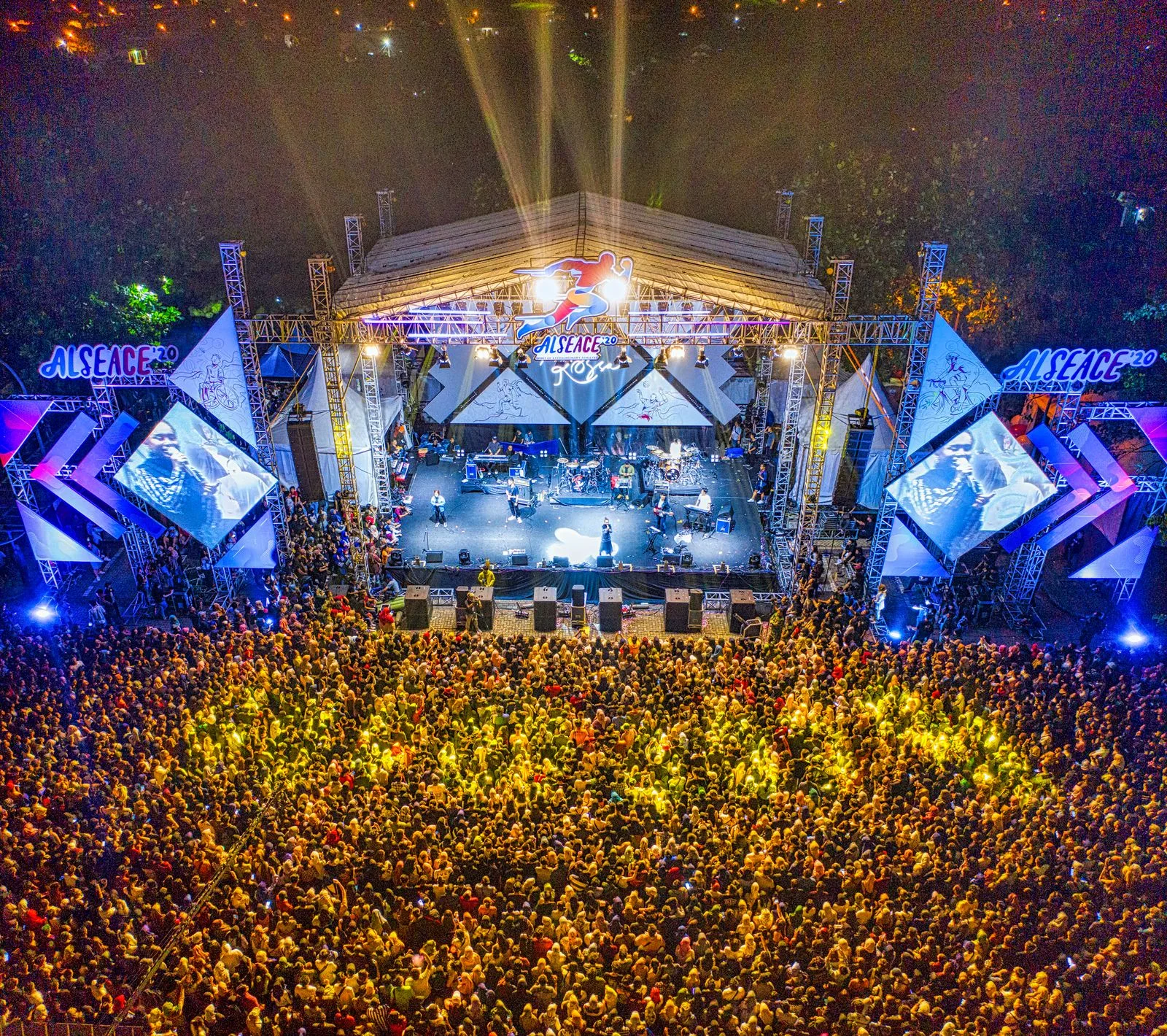 An outdoor concert with stage lights and a large audience