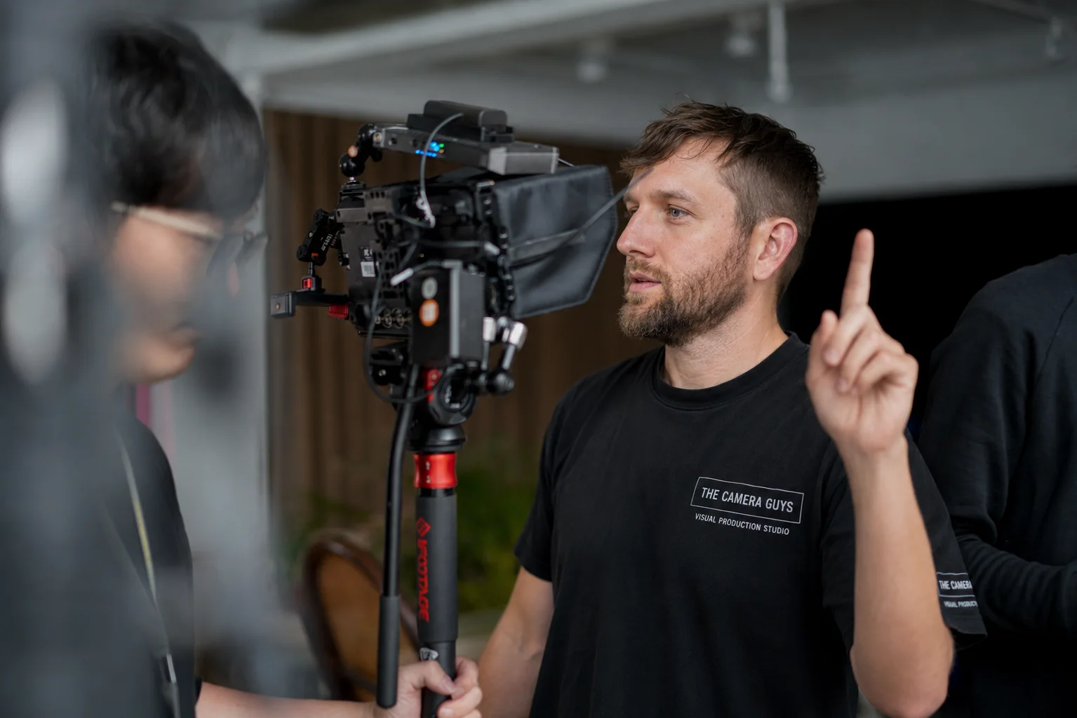 Videographer giving direction beside a tripod-mounted cinema camera