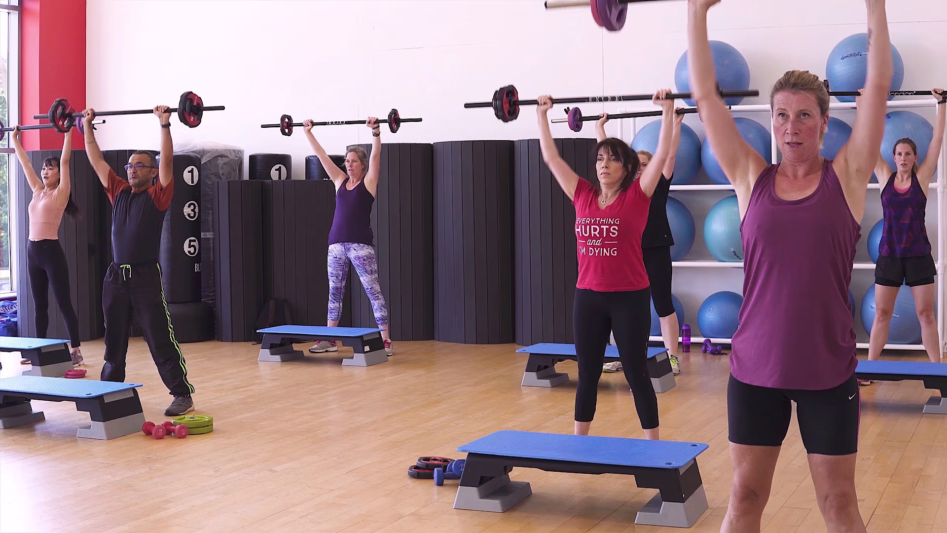 Group fitness class raising barbells overhead