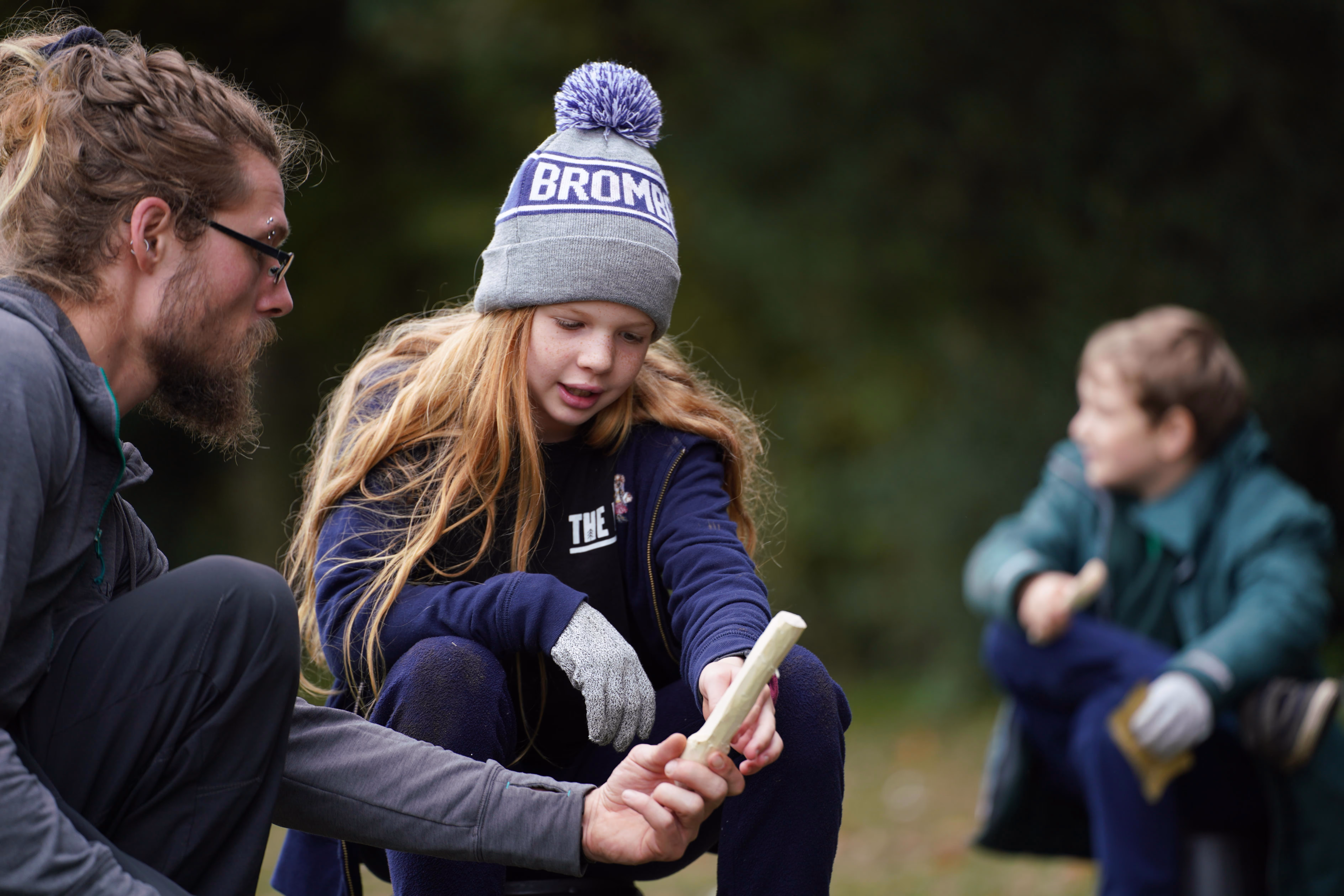 Instructor guiding a child through an outdoor bushcraft task