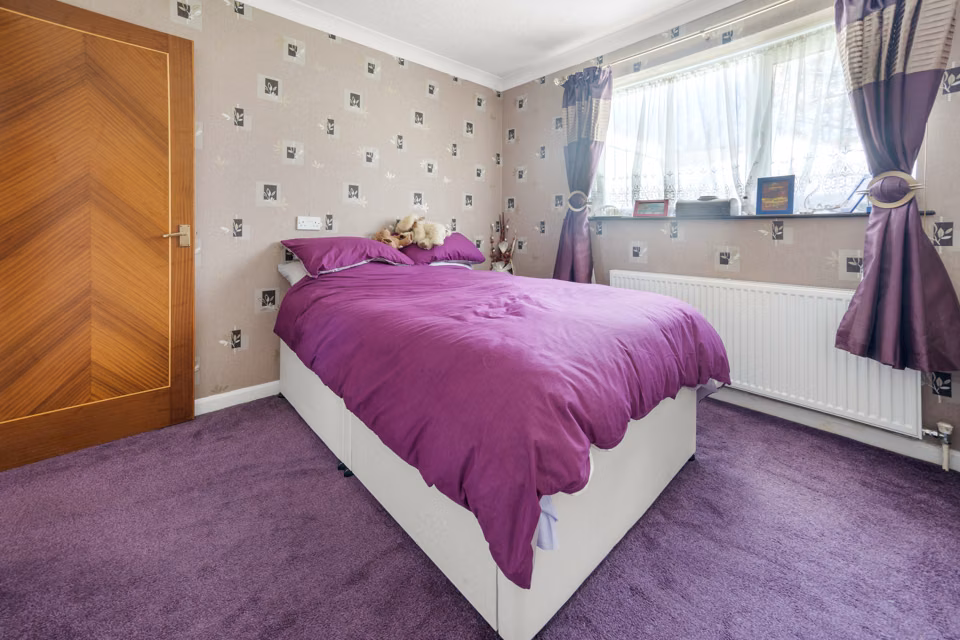 Bedroom with a purple bedspread below the window — 13 Furness Close