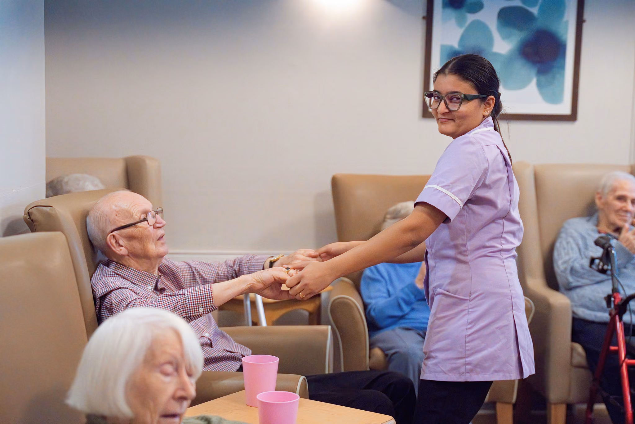 A carer holding a seated resident’s hands in Eastham’s living room