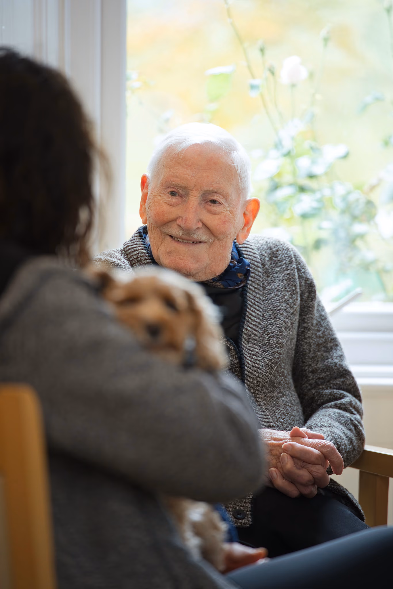 A resident smiling at the dog’s handler beside a window