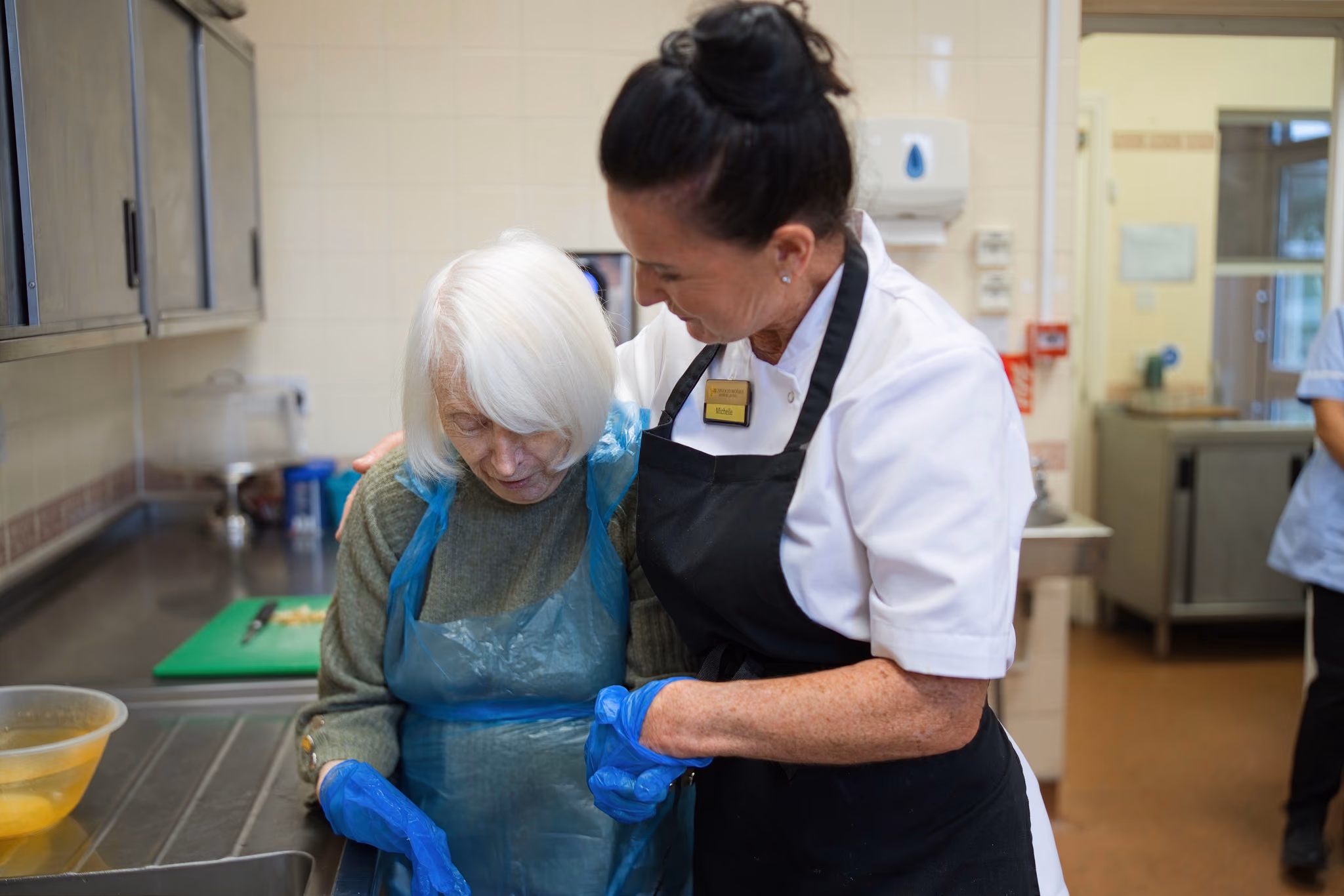 A resident and staff member working together at the kitchen sink