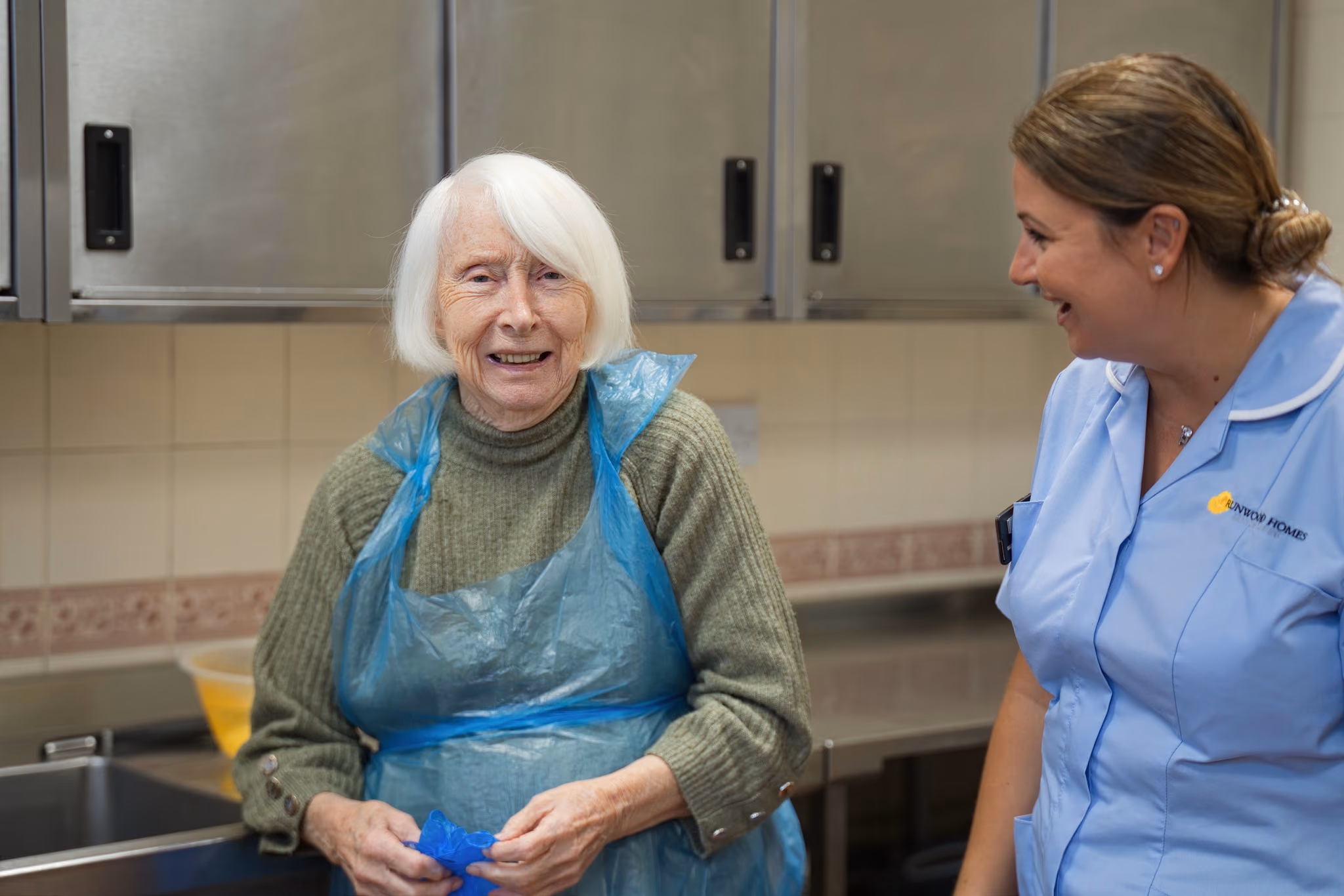 A resident smiling with a carer in the kitchen