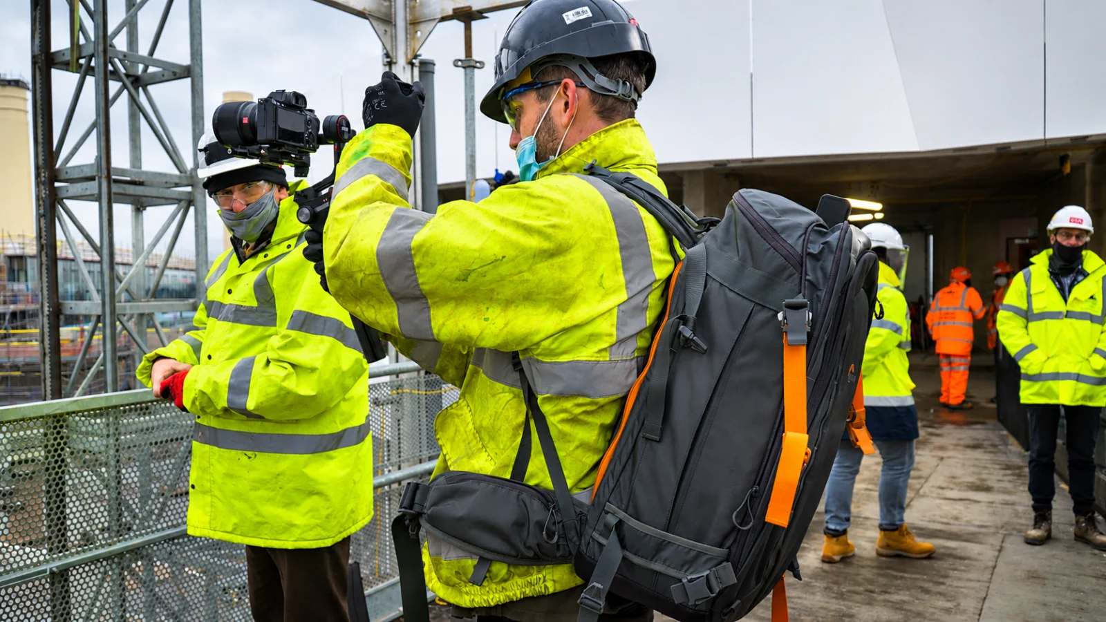 Videographer in high-visibility clothing carrying camera kit on a construction site