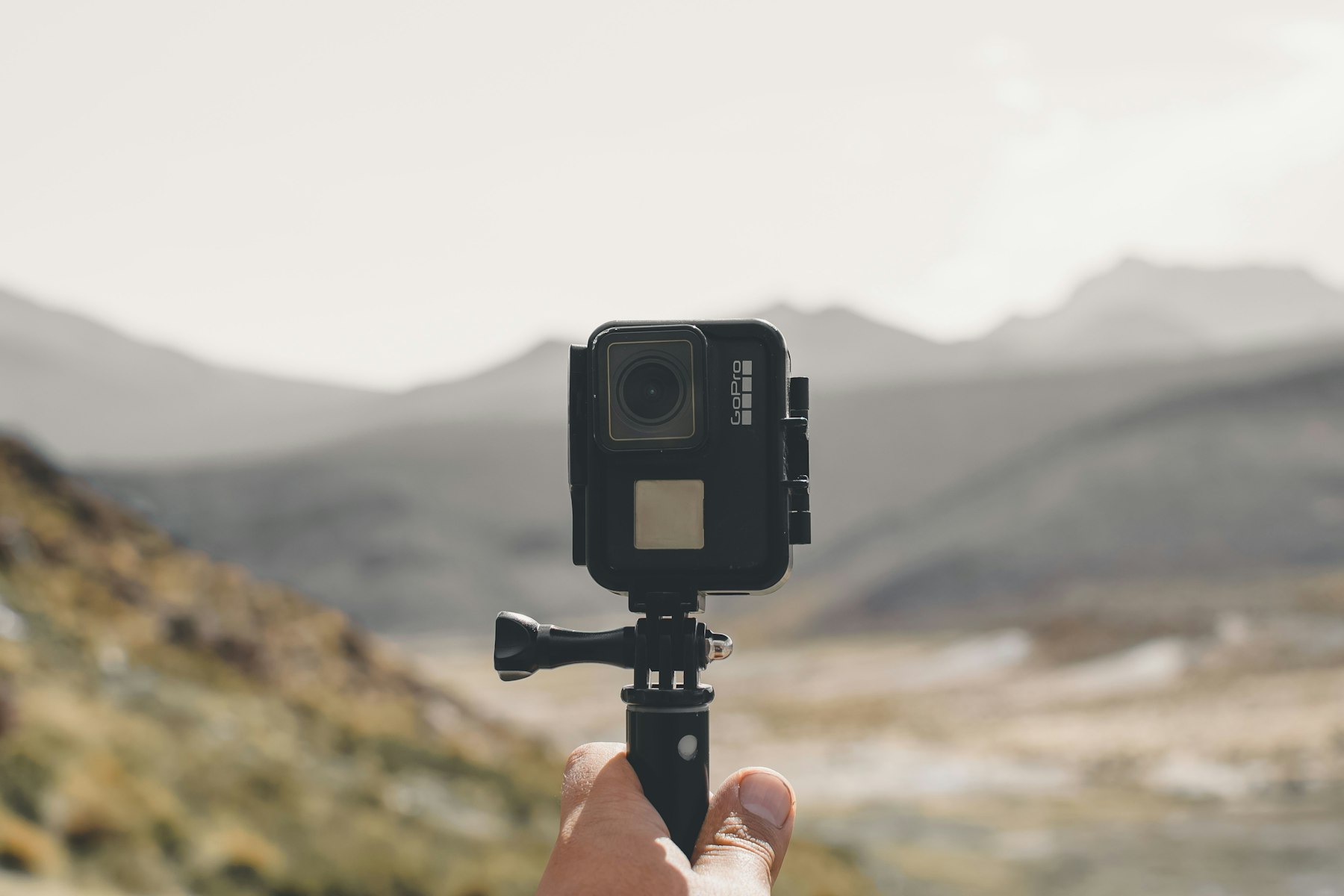 An action camera on a small tripod held up against a mountain landscape