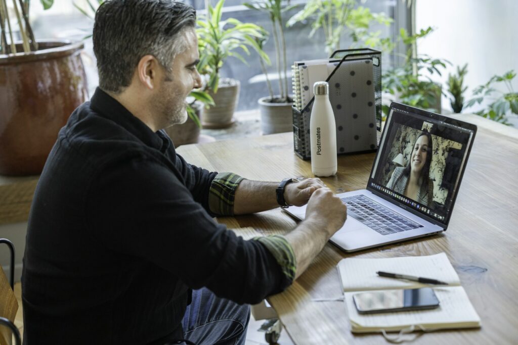 A man at a desk talking to a colleague on a laptop video call
