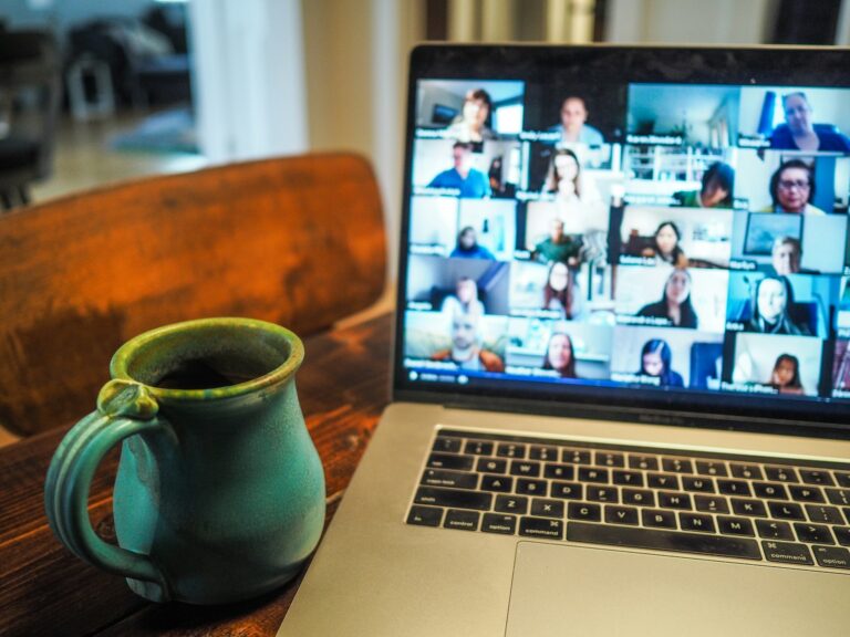 A laptop on a wooden table showing a Zoom gallery view of a group video call