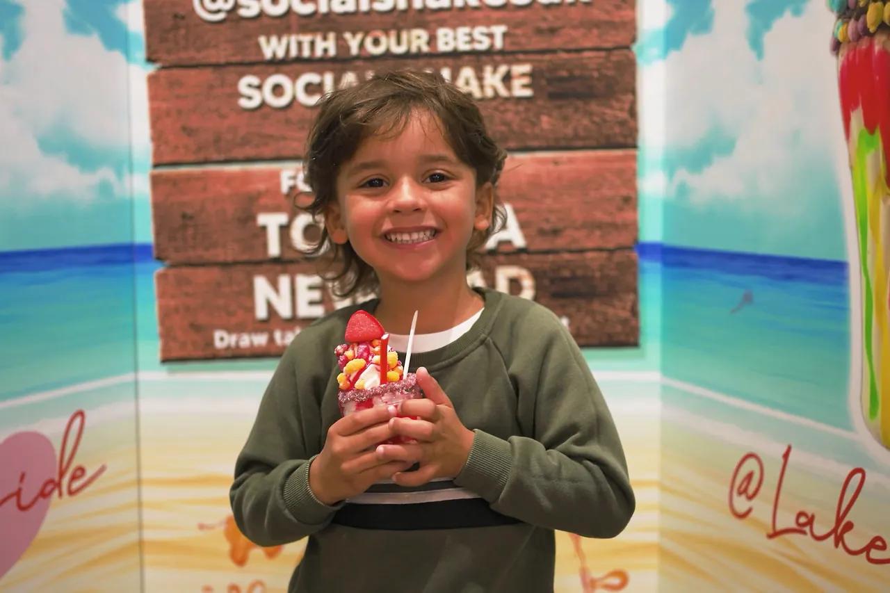 Child smiling with a shake in front of a mural
