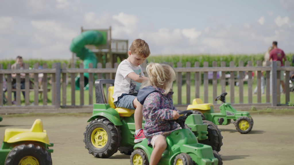 Children riding green and yellow toy tractors at Southwold Maize Maze